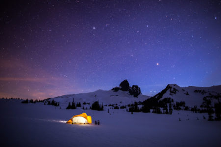 Glowing yellow tent with stars and Black Tusk in the background winter camping in Garibaldi Provincial Park near Whistler, BC