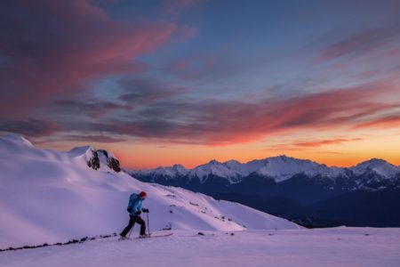 Skier skinning touring splitboarding up a snowy slope in the backcountry near Whistler Blackcomb Tantalus range mountain sunset alpenglow.